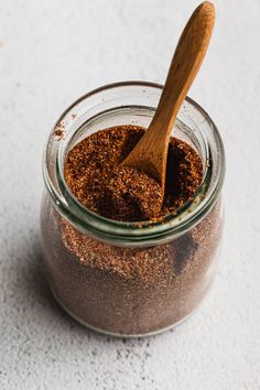 a wooden spoon in a glass jar filled with ground cinnamon on a white counter top