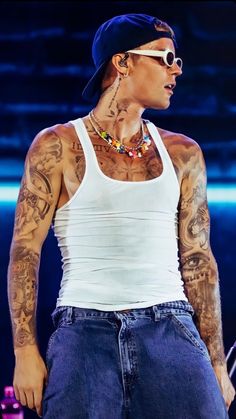 a man with tattoos on his arms and chest standing in front of a microphone wearing jeans