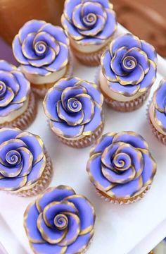 several cupcakes with purple frosting and gold swirl designs on them sitting on a white plate