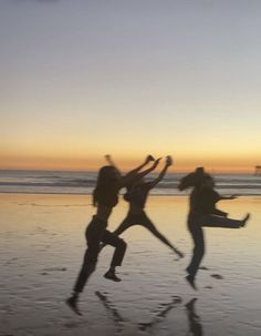 three people jumping on the beach at sunset