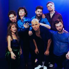 a group of people standing next to each other in front of a blue wall with their arms around one another