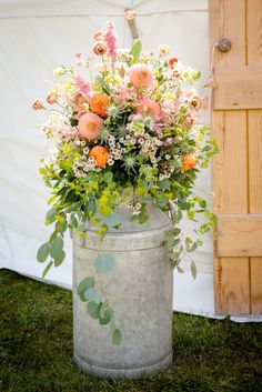 a large metal bucket filled with flowers on top of a grass covered field next to a wooden door