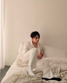 a young man sitting on top of a bed with white sheets and striped comforter