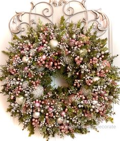 a christmas wreath with ornaments hanging on the front door, decorated with silver and pink baubies