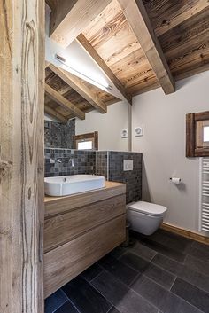 a bathroom with a toilet, sink and wood paneled ceiling in the corner is shown