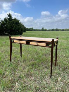 a wooden desk sitting in the middle of a grass field with trees in the background