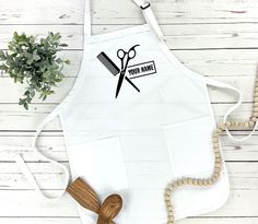 a white apron with scissors on it next to a wooden bead and a plant