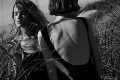 black and white photograph of two women standing in tall grass looking at each other with their backs to the camera