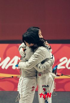 two women hugging each other in front of a red wall with an olympic sign behind them