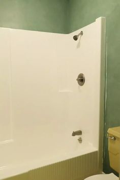 a white toilet sitting next to a bath tub in a green walled bathroom with an open shower door