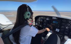 a woman wearing headphones sitting in the cockpit of a plane with an alien mask on her face