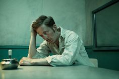 a man sitting at a table with his hand on his head and looking down, in front of him