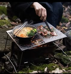 a person is cooking food on an outdoor grill with chop sticks and broccoli