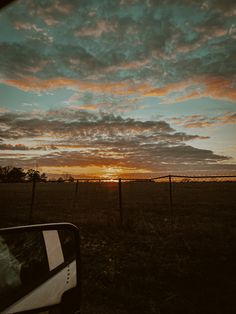 the sun is setting over an open field with a wire fence and trees in the background