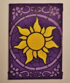 a purple and yellow tile with a sun design on it's side, hanging from the wall