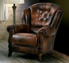 a brown leather chair sitting on top of a hard wood floor next to a lamp