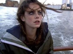 a woman is sitting on a boat in the water looking off into the distance with her hair blowing in the wind