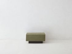 a small green bench sitting on top of a white floor in front of a wall