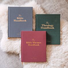 three books sitting on top of a fluffy white blanket next to each other with the words bible handbook written in gold