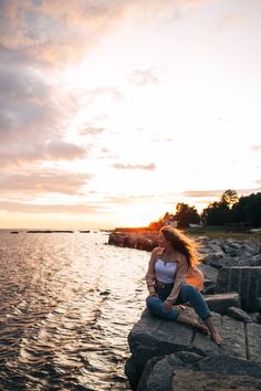 a woman sitting on top of a rock next to the ocean