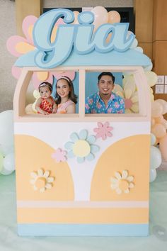 a man and woman are sitting in a fake bus with flowers on the side, surrounded by balloons