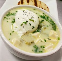 a bowl of soup with cheese and sour cream in it on a plate next to bread