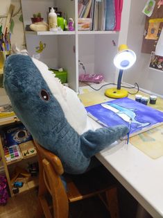 a stuffed shark sitting on top of a wooden chair in front of a computer desk