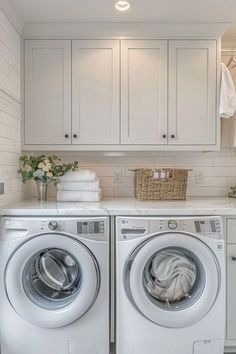 a washer and dryer in a white laundry room with cabinets on either side