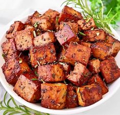 a white bowl filled with cooked tofu and garnished with herbs