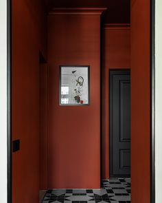 an empty room with black and white checkered floor, red walls and framed pictures on the wall