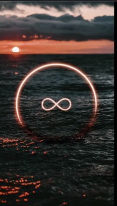 an infinite symbol floating in the ocean at sunset