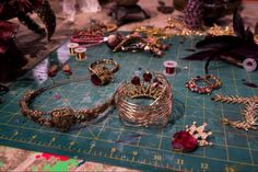 many different bracelets and rings are on a cutting board next to thread spools