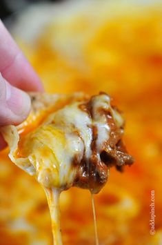 a hand holding a piece of cheese covered pizza