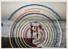 a group of people standing on top of a beach next to the ocean with colorful hula hoops