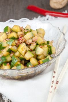 a glass bowl filled with cucumber salad next to chopsticks