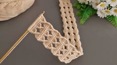 a crocheted piece of cloth next to a knitting needle and some daisies