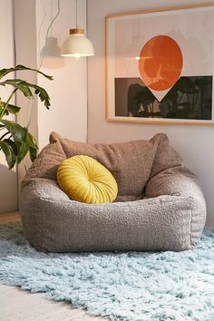 a dog bed with a yellow pillow on top of it next to a potted plant