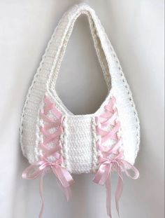 a crocheted white purse with pink bows on the front and bottom, hanging from a hook