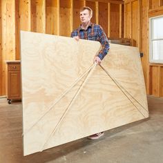 a man holding a large piece of plywood in the middle of a room with wood paneling