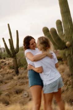 two women hugging each other in front of a cactus