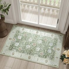 a green rug on the floor in front of a door with flowers and potted plants