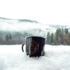 a black coffee cup sitting on top of snow covered ground