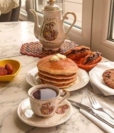 a table topped with pancakes and muffins next to a cup of coffee