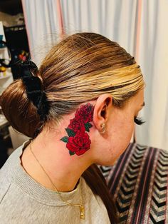 a woman with a red rose tattoo on her left side behind her ear, looking at the camera