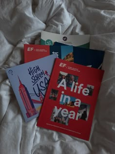 three books laying on top of a bed next to each other in front of a white sheet