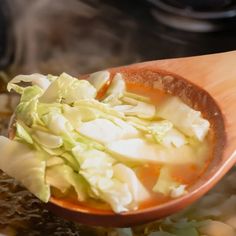 a wooden spoon filled with cabbage and soup on top of a stovetop oven burner