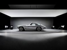 a black and white photo of a car in a dark room with spotlights on the floor