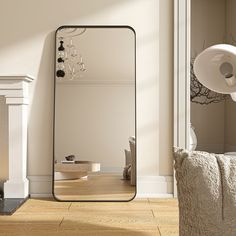 a large mirror sitting on top of a wooden floor next to a white chair and fireplace