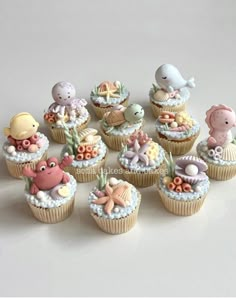 cupcakes decorated with sea animals and seashells are arranged on a white surface