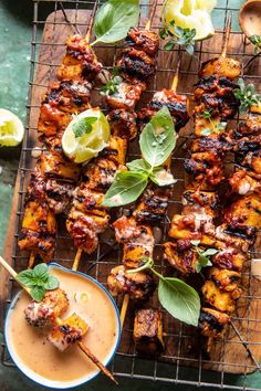 grilled chicken skewers on a grill with dipping sauce and fresh basil leaves